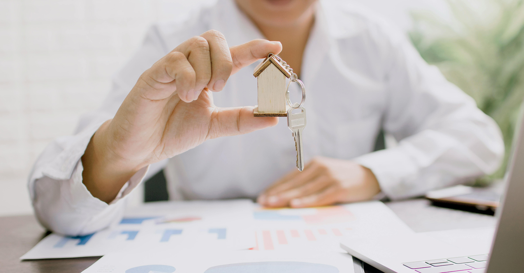 man holding a small plastic house with a key hanging in front of it